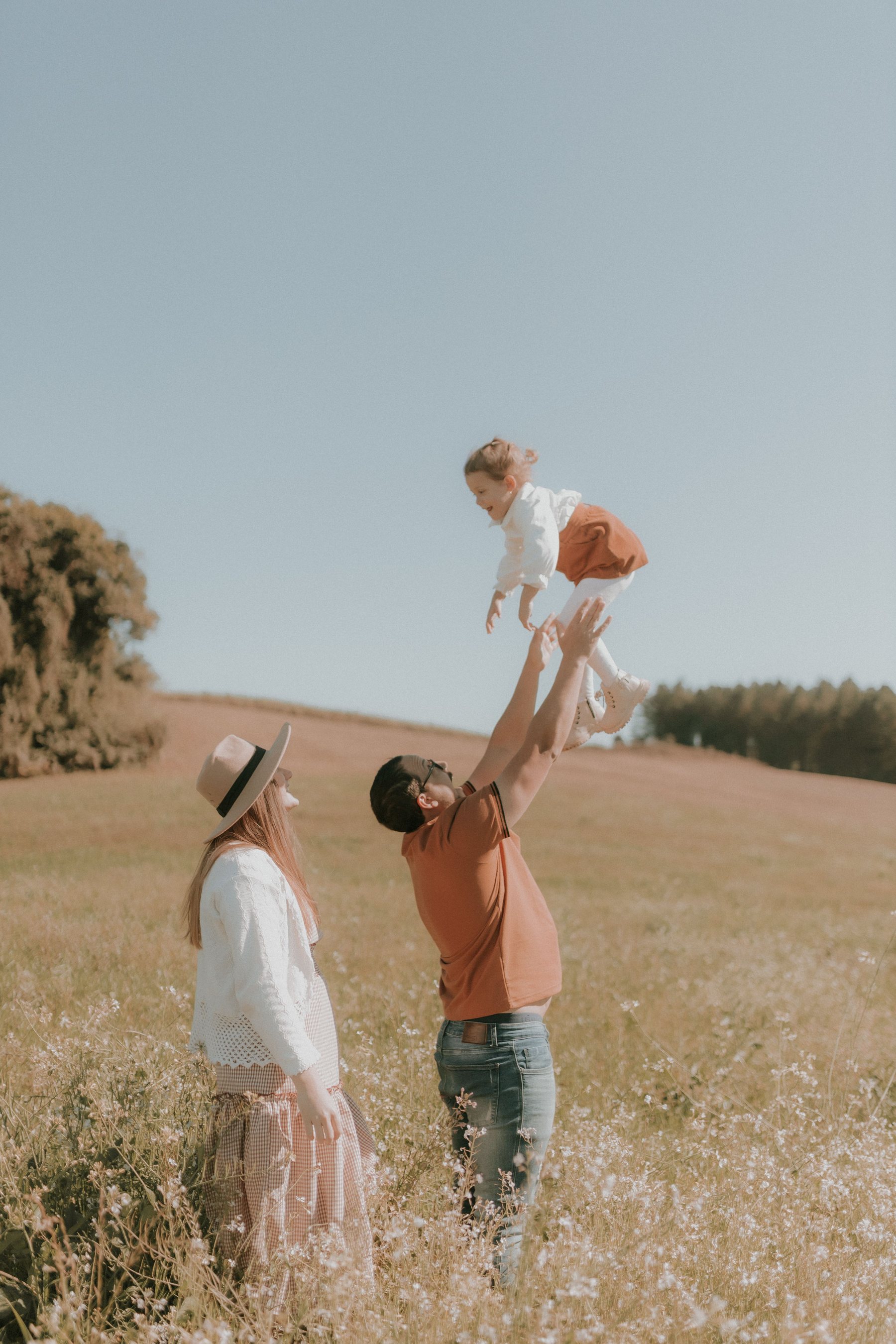 Parents in a sunlit field lifting their child into the air.